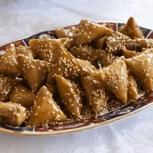 Assiette de Briwat D'amande, une pâtisserie marocaine en forme de triangle, garnie d'une farce à base d'amandes, de sucre et d'épices, frite jusqu'à obtenir une couleur dorée et croustillante.