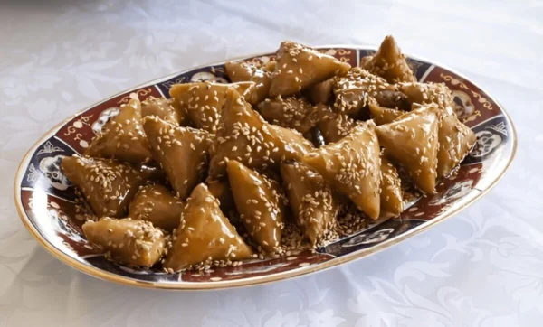 Assiette de Briwat D'amande, une pâtisserie marocaine en forme de triangle, garnie d'une farce à base d'amandes, de sucre et d'épices, frite jusqu'à obtenir une couleur dorée et croustillante.